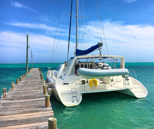 Spacious white catamaran moored at a rustic wooden dock, surrounded by vivid blue Caribbean waters.